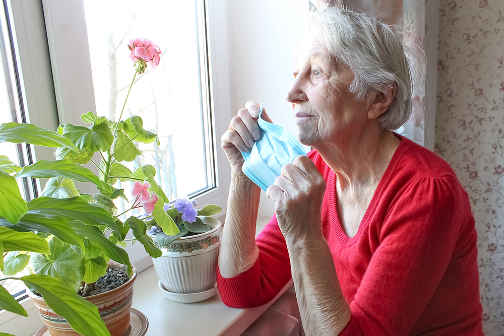 senior lady holding mask looking longingly out window