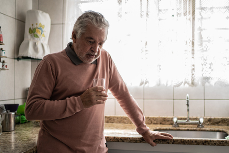 A depressed man stands in the kitchen staring at the ground, a reminder to safeguard mental health after a heart issue.